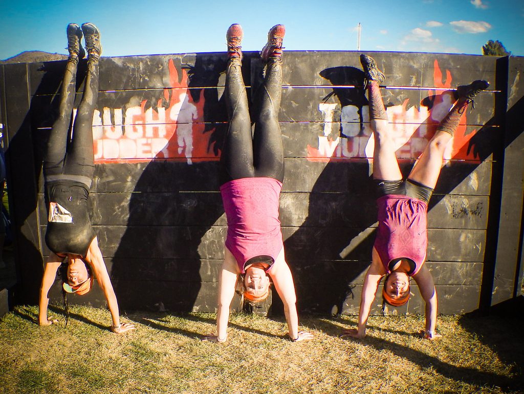 Three people doing handstands in front of a wall with the tough mudder logo