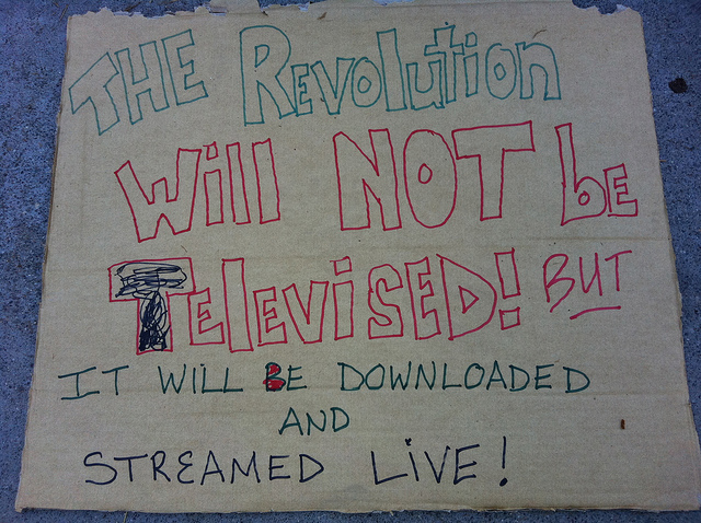 A handwritten protest sign, reading: The revolution will not be televised but it will be downloaded and streamed live